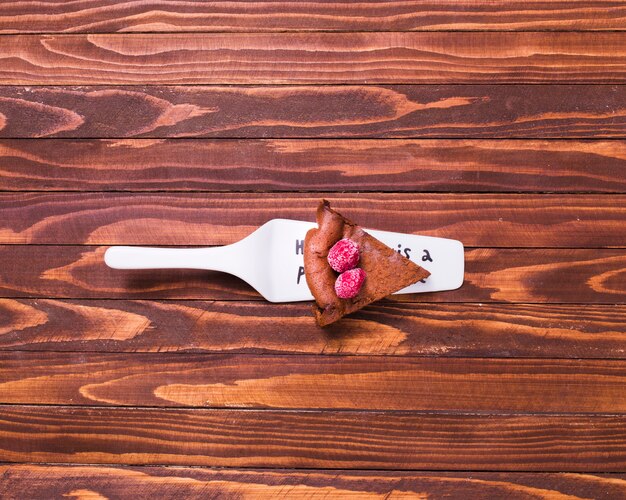 Serving chocolate cake slice on white spatula over the wooden surface