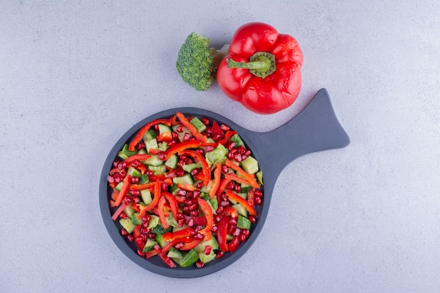 Serving pan of vegetable salad next to a bell pepper and a broccoli on marble background. High quality photo