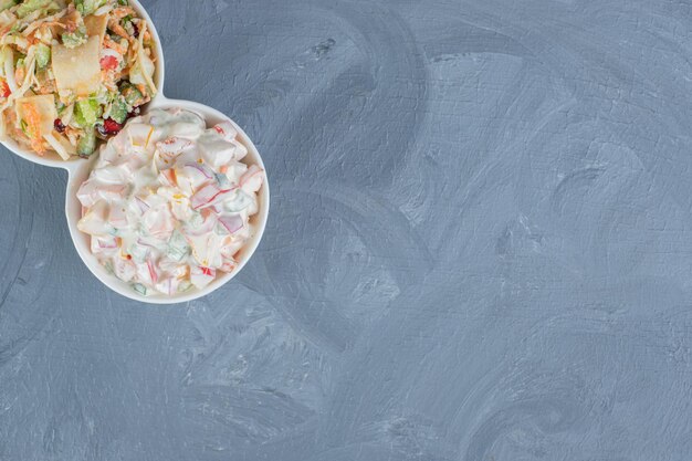 Serving platter with portions of olivier and mixed vegetable salads on marble table.