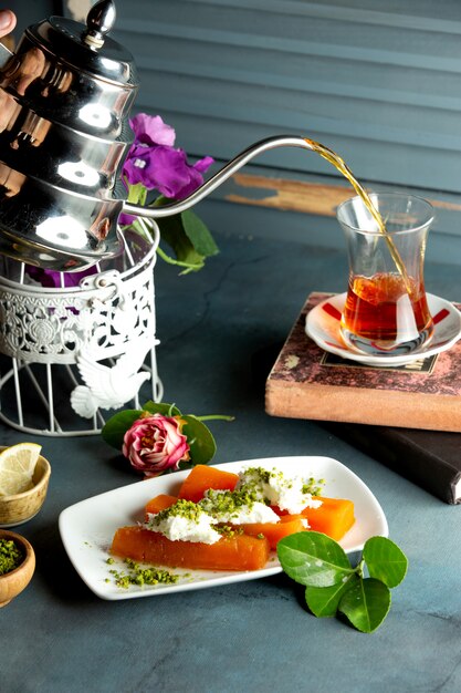 A serving of quince dessert topped with cream and pistachio served with black tea