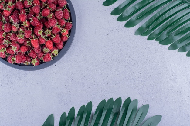 Serving tray full of raspberries next to decorative leaves on marble background. High quality photo