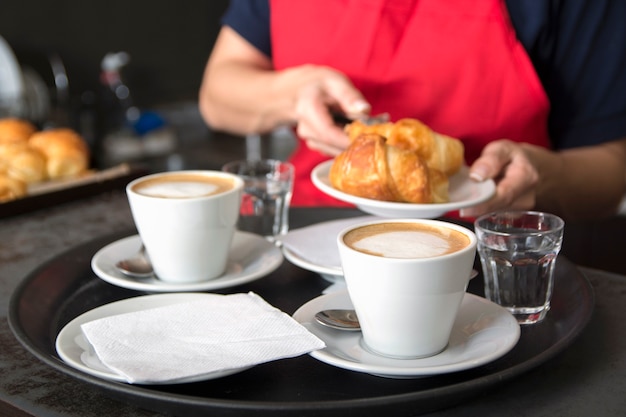 Serving two coffee cups in front of the waitress placing croissant in the plate