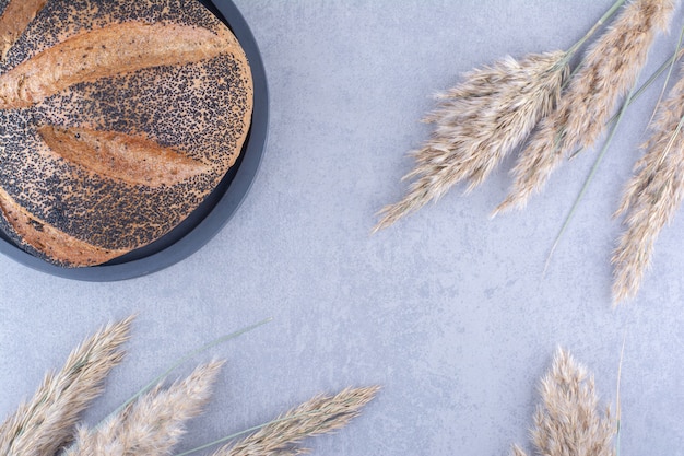 Sesame coated bread loaf on a platter next to stalks of dried feather grass on marble surface