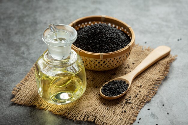 Sesame oil and raw black sesame seeds on dark background