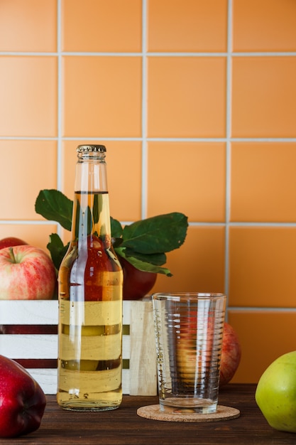 Set of apple juice and apples in a box on a wooden and orange tile background. side view. space for text