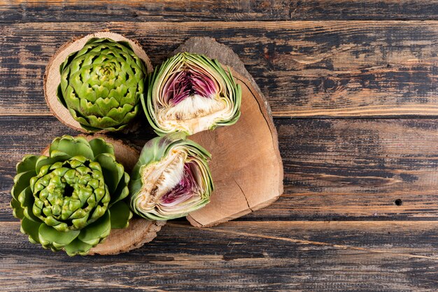 Set of artichokes and slices on small stubs and dark wooden background. top view.