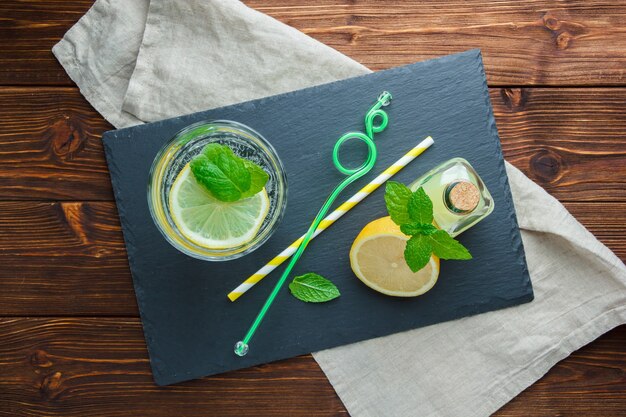 Set of black cardboard, straws, juice bottles and sliced lemon in a bowl on a wooden surface. top view.