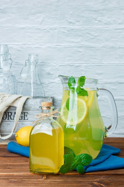 Set of blue cloth, empty bottles and carafe of lemon juice on a wooden and white surface. side view. free space for your text