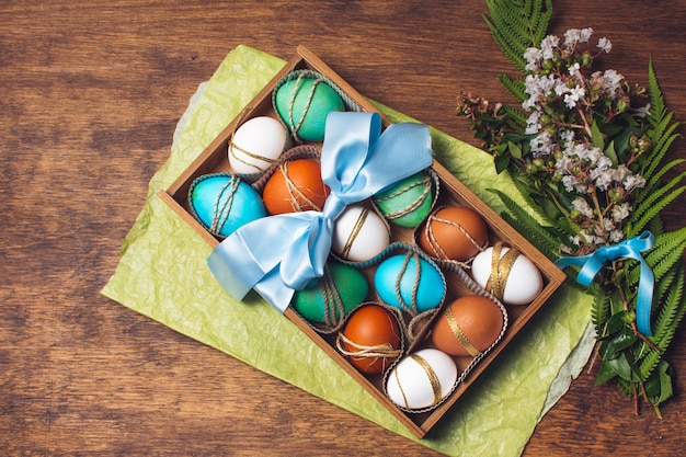 Set of bright eggs in box on craft paper near bunch of plants