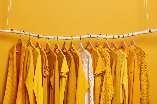 Set of bright yellow clothes and one white sweater on hangers. Collection of womens attires to wear. Variety of outfits for warm and hot weather.