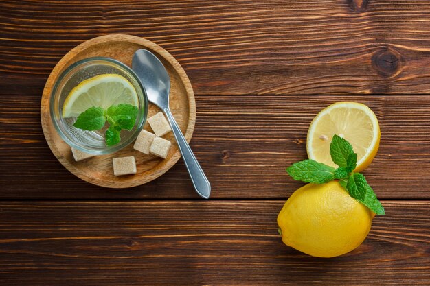 Набор коричневого сахара и дольки лимона в деревянной тарелке и лимона и листьев на деревянном столе