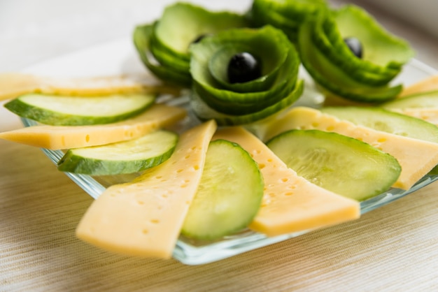 Set of cheese, cucumber and avocado with olives on dish on table
