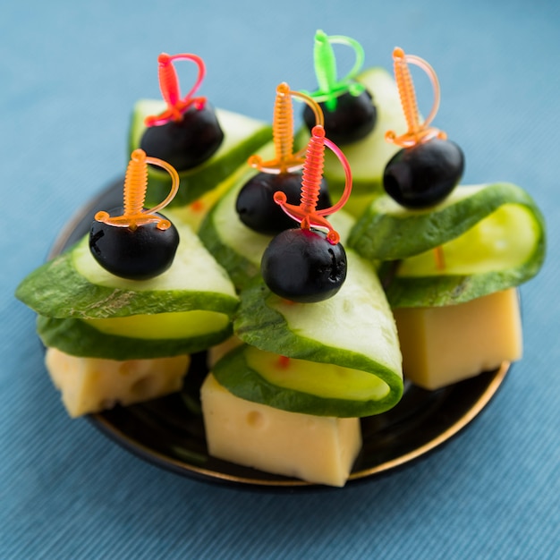 Set of cheese, olive and cucumber on plastic skewer on plate