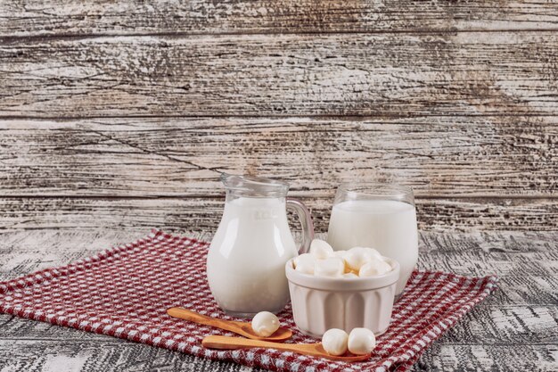 Set of cheese and wooden spoon and bottles of milk on a gray wooden and picnic cloth background. side view. space for text