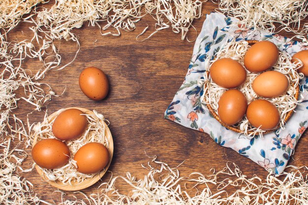 Set of chicken eggs in bowls on flowered material between tinsel on board