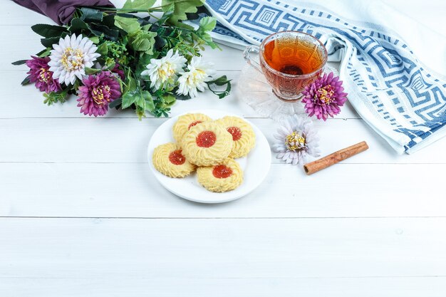 シナモン、お茶、キッチンタオル、クッキー、白い木の板の背景の花。ハイアングルビュー。