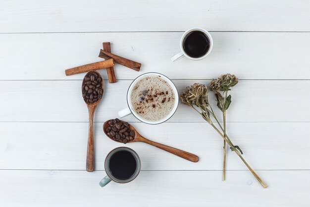 Набор кофейных зерен, палочек корицы, сушеных трав и кофе в чашках на деревянном фоне. вид сверху.
