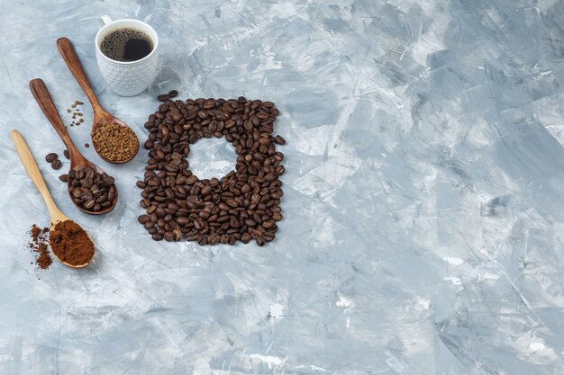 Набор кофейных зерен, растворимого кофе, кофейной муки в деревянных ложках и чашки кофе на светло-синем мраморном фоне. высокий угол обзора.