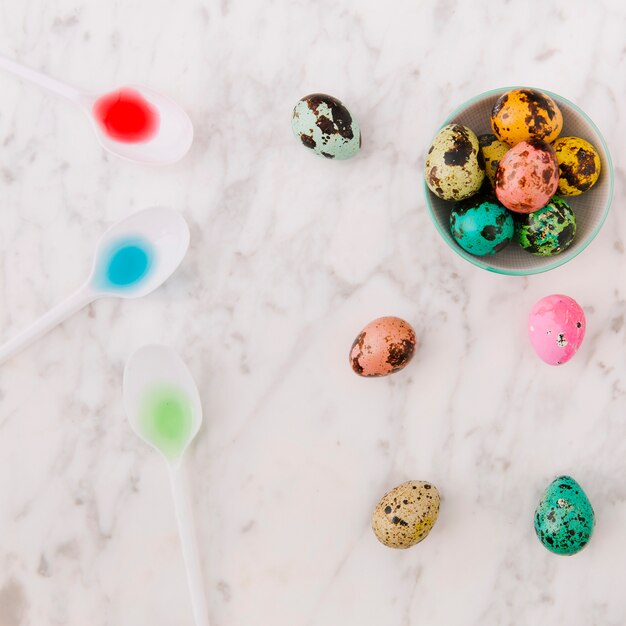 Free photo set of colourful quail easter eggs in bowl near spoon with dyes