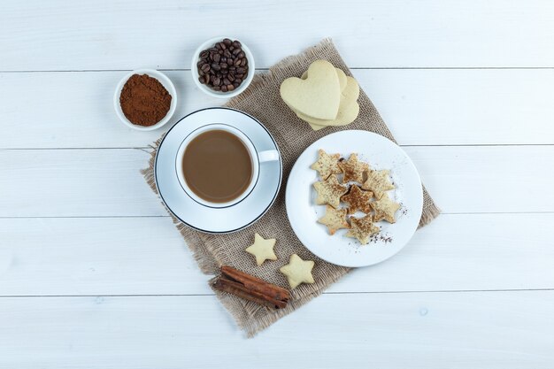 クッキー、シナモンスティック、コーヒー豆、挽いたコーヒーとコーヒーのセットは、木製と袋の背景のカップに。上面図。