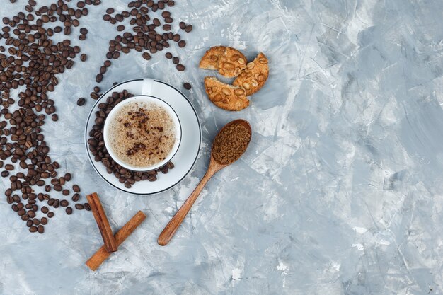 Набор печенья, кофейных зерен, молотого кофе, палочек корицы и кофе в чашке на сером гипсовом фоне. вид сверху.