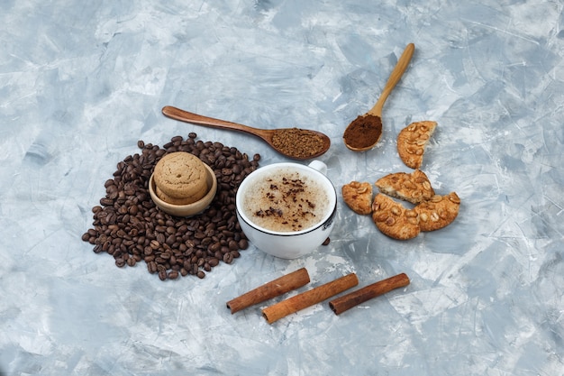 Set di biscotti, chicchi di caffè, caffè macinato, bastoncini di cannella e caffè in una tazza su uno sfondo grigio sgangherato. vista ad alto angolo.