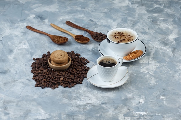Set of cookies, coffee beans, grinded coffee and coffee in cups on a grungy grey background. high angle view.
