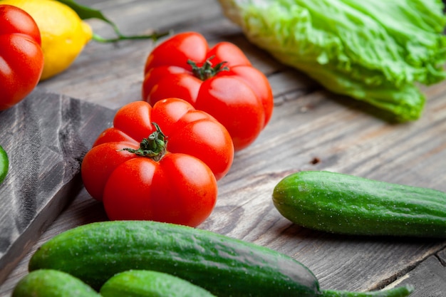 Set of cucumber, lettuce, lemon and tomatoes in a cutting board on a dark wooden background. high angle view.