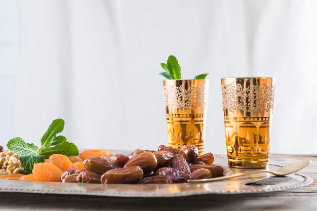 Set of cups with plant twigs and dried fruits on tray on table