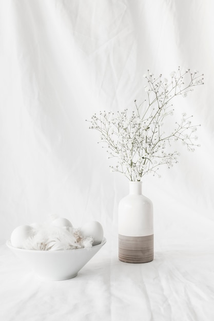 Set of Easter eggs and quills in bowl near plant branches in vase