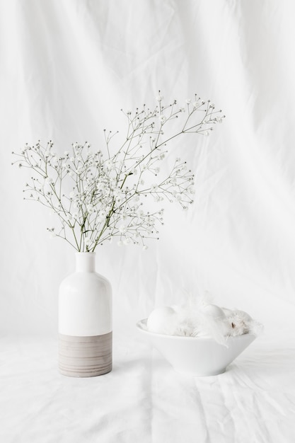 Set of Easter eggs and quills in bowl near plant twigs in vase