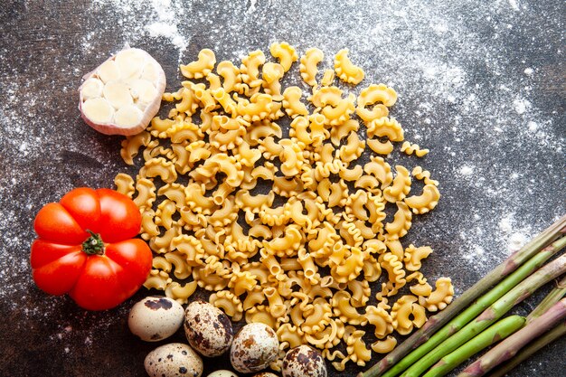 Set of eggs, tomato, asparagus and garlic and macaroni on a dark textured background. top view.