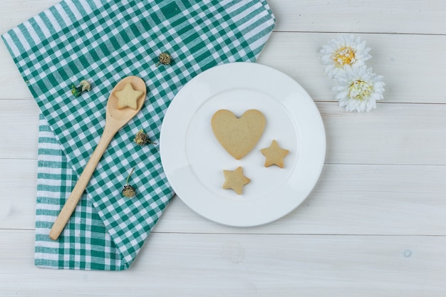 Set of flowers and cookies in plate and wooden spoon on wooden and kitchen towel background. flat lay.