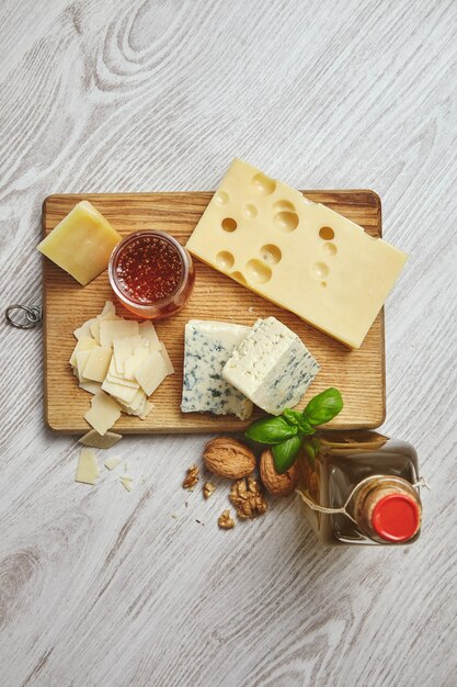 Set of four cheeses on rustic cutting board. Served for breakfast with extra virgin olive oil in vintage bottle, rustic honey and walnuts with basil leaves