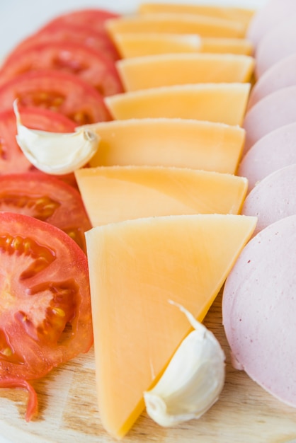 Set of fresh cheese near tomatoes and lunch meat on board