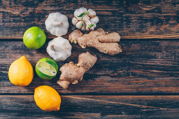 Foto gratuita set di zenzero, aglio e limoni verdi e gialli su un fondo di legno scuro. disteso.