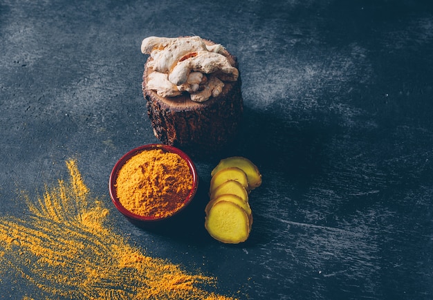 Set of ginger and slices and ginger powder in a bowl and on a wood stub on a dark textured background. high angle view. space for text