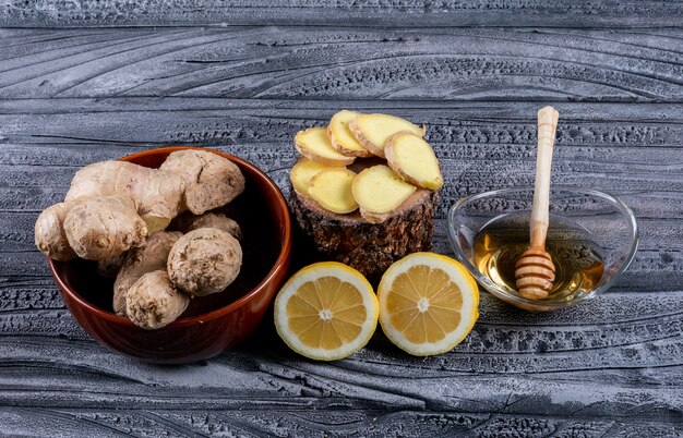 Set of ginger slices, lemon and ginger and honey in a bowls on a dark wooden background. top view.