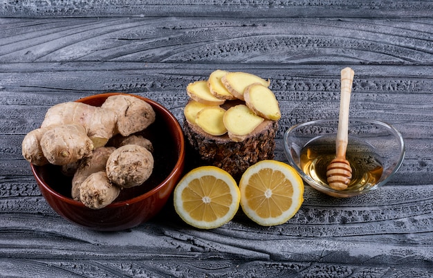 Set of ginger slices, lemon and ginger and honey in a bowls on a dark wooden background. top view.