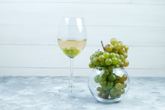 Set of a glass of wine and green grapes in a glass pot on grungy grey and wooden background. side view.