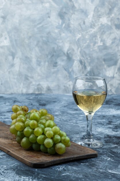 Set di bicchiere di vino e uva bianca su un tagliere su uno sfondo di marmo blu scuro e chiaro. avvicinamento.