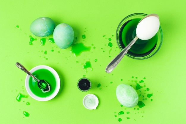 しみ、スプーン、染料の液体の間の緑のイースターエッグのセット