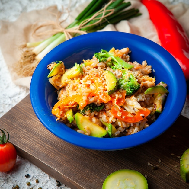 Set of green onions and pepper and delicious meal in a blue plate on a wood, red cloth and white textured background. high angle view.