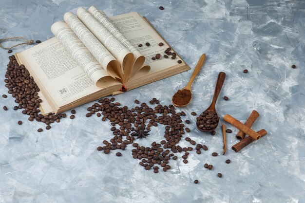 Набор измельченного кофе, книги, палочек корицы и кофейных зерен в деревянной ложке на шероховатом сером фоне. высокий угол обзора.
