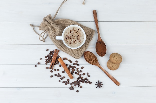 Набор измельченного кофе, специй, кофейных зерен, печенья и кофе в чашке на фоне деревянных и мешков. вид сверху.