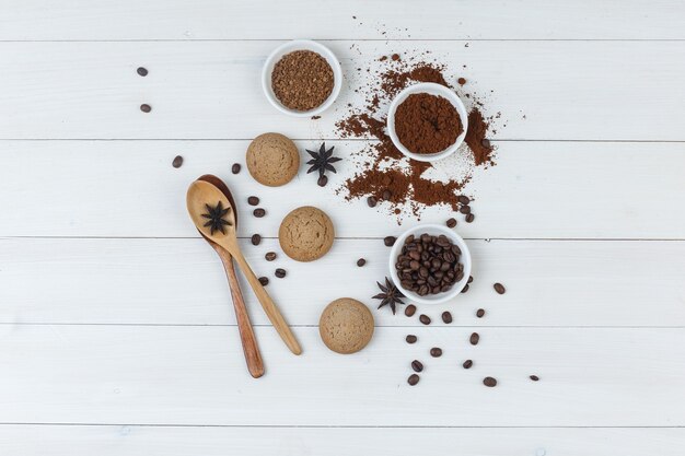 Набор измельченного кофе, специй, печенья, деревянных ложек и кофейных зерен в миске на деревянном фоне. вид сверху.