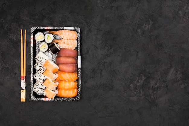 Set of healthy asian rolls arranged in tray and sticks over black background