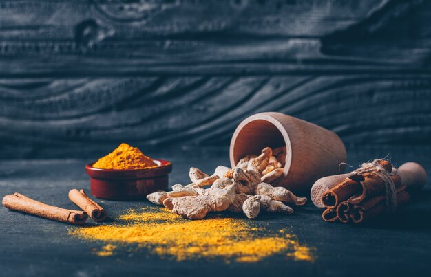 Set of herb grinder, ginger and dry cinnamon and ginger powder in a tea cups on a dark textured background. side view. space for text