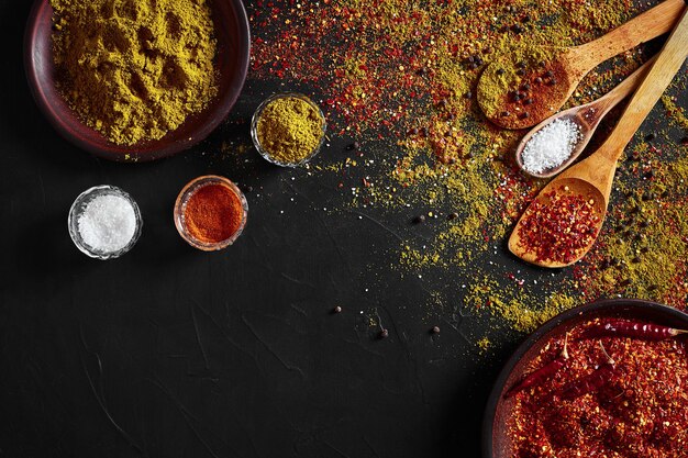 Set of indian spices on black background - green cardamom, turmeric powder, coriander seeds, cumin, and chili, top view. Copy space. Flat lay