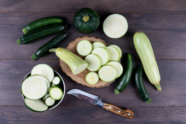 Set of knife and other zucchinis in a bowl and around and sliced zucchinis on a dark wooden table. flat lay.